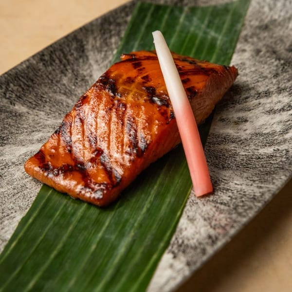 AquaSan's grilled salmon with a pink and white garnish, served on a banana leaf and stone plate.