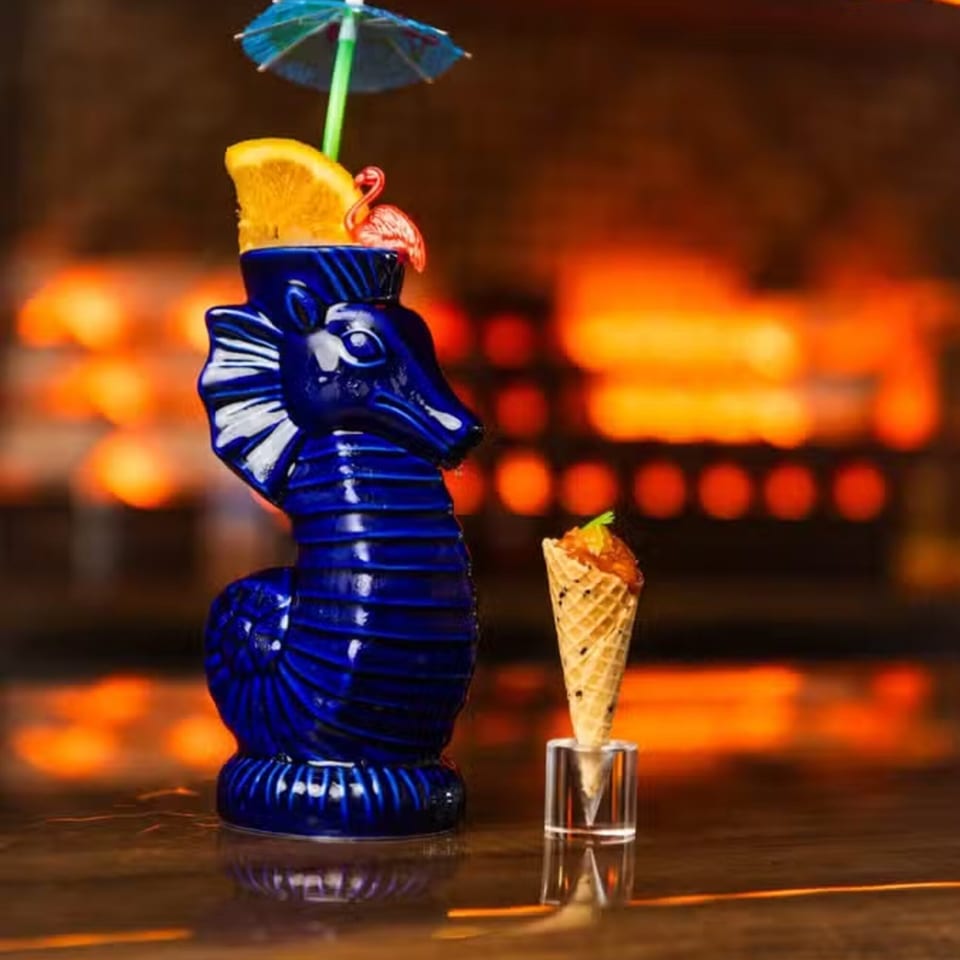 AquaSan's blue seahorse cocktail with an orange slice, umbrella, and flamingo, next to a mini ice cream cone.