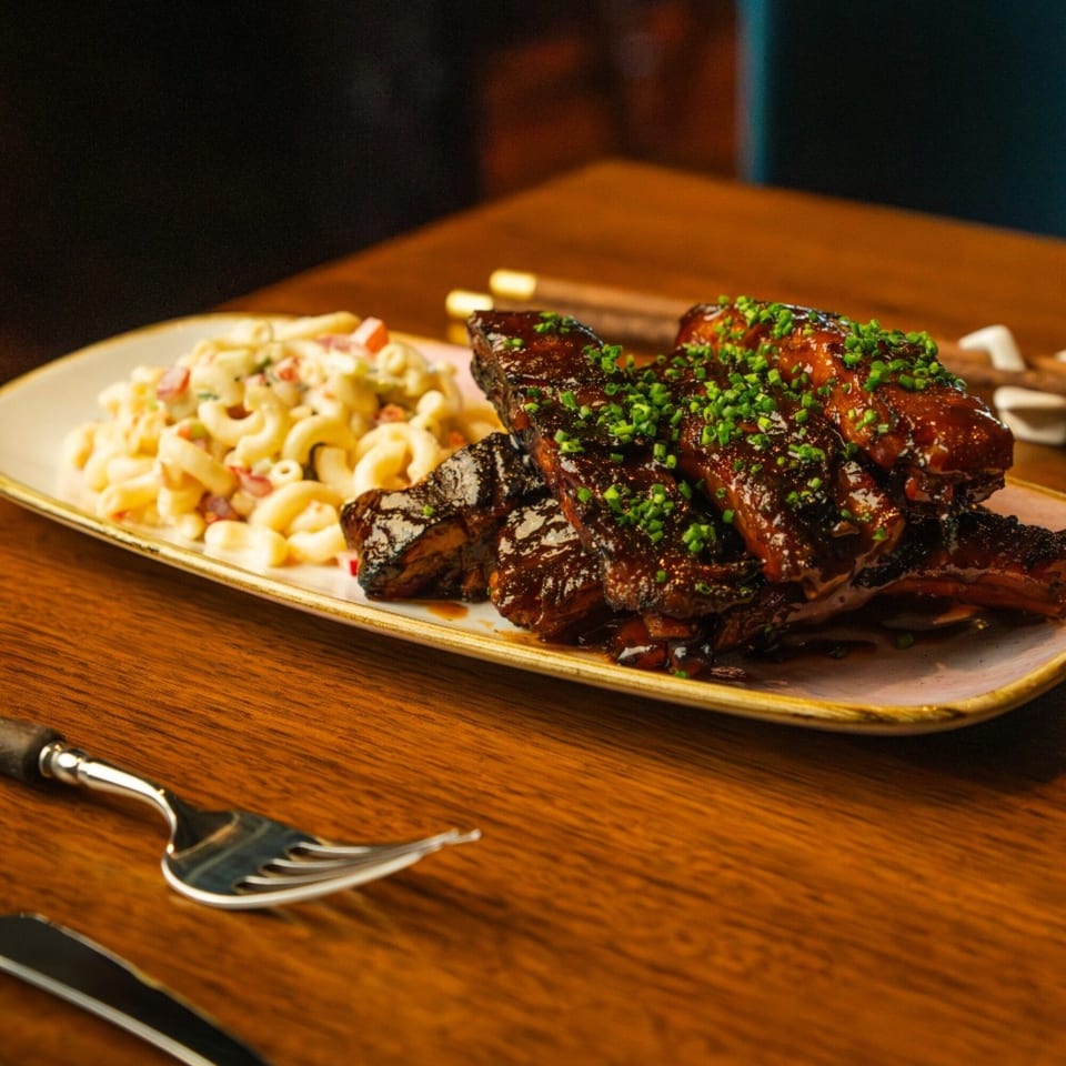 AquaSan's Asian-style ribs with a rich glaze and chives, served with macaroni salad on a wooden table.