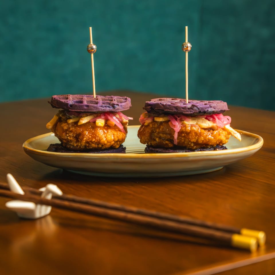 Two AquaSan purple waffle sliders with fried chicken, pickled onions, and fries on a plate.
